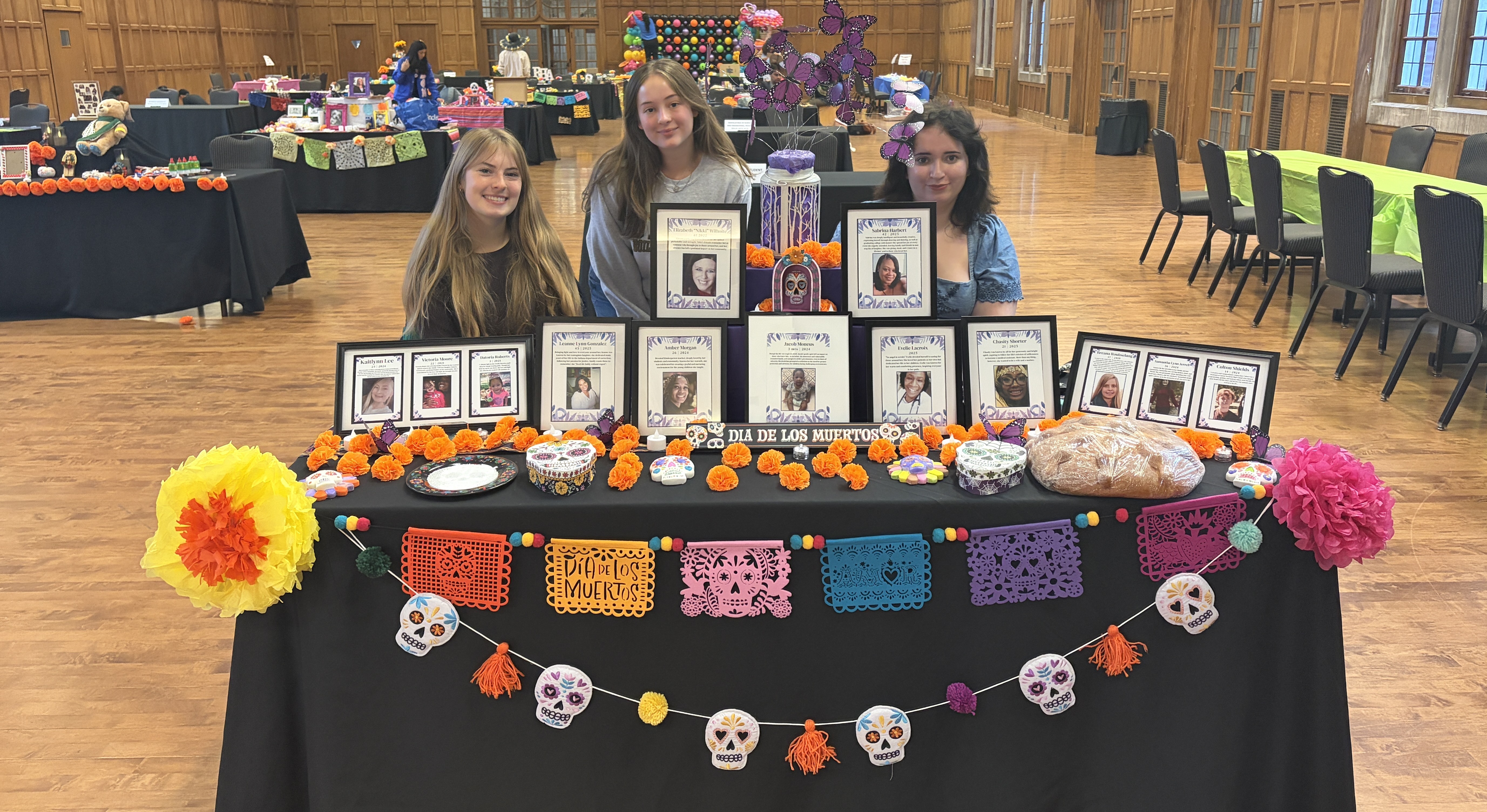 A photo of three student volunteers at a table decorated for Dia De Los Muertos.